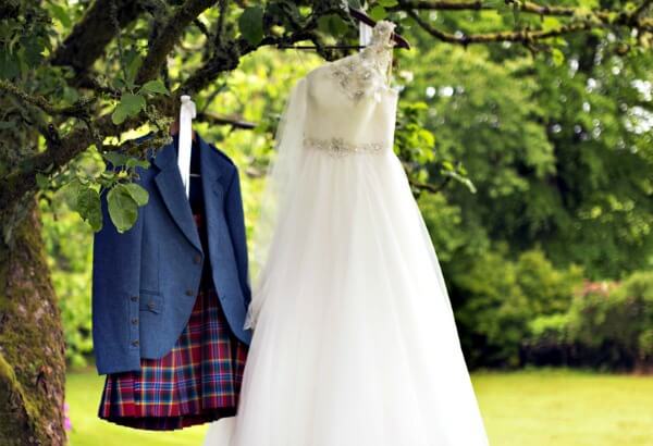 Scottish wedding dress and grooms kilt hanging from a tree outdoors